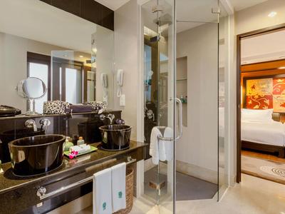 Área de baño moderna con lavabos, espejo y acceso abierto al dormitorio en una habitación de hotel.