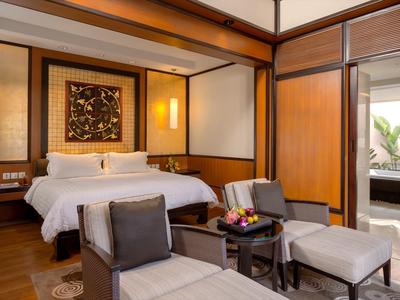 Habitación de hotel moderna con una cama grande, dos sillones y acceso a un balcón con plantas.