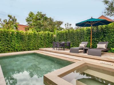 Área de piscina moderna con tumbonas, mesa y sombrilla rodeada de seto verde.