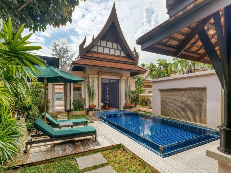 Traditionelles thailändisches Haus mit blauem Pool, grünen Pflanzen und Liege unter Schirm.