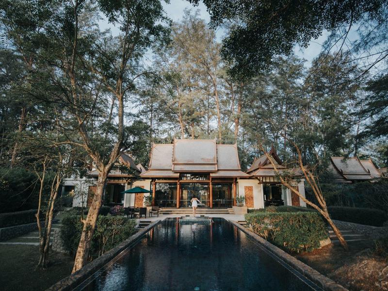 Ein großes Haus mit Holzfassade umgeben von Bäumen und einem langen, schmalen Pool im Vordergrund.