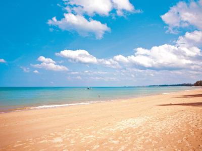 Szeroka piaszczysta plaża z niebieskim niebem i kilkoma chmurami nad spokojnym morzem.