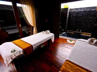 Pokój zabiegowy z dwoma stołami do masażu i ciemną drewnianą podłogą w hotelowym spa.