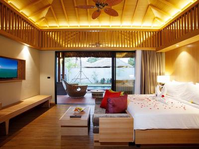 Nowoczesny pokój hotelowy z drewnianą podłogą, podwójnym łóżkiem i widokiem na taras z wiszącym fotelem i morzem.