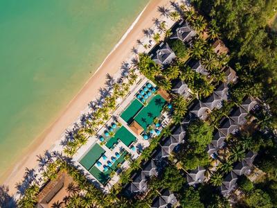 Widok z lotu ptaka na ośrodek nad brzegiem morza z basenami otoczonymi palmami.