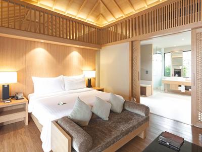 Lichte hotelkamer met groot bed, bank en open toegang tot badkamer met badkuip.