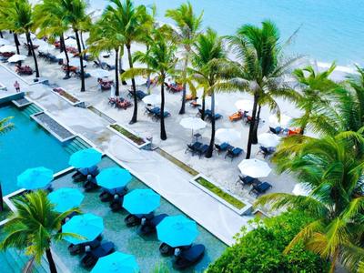 Luksusowy obszar basenu z parasolami obok białej piaszczystej plaży i turkusowego morza.