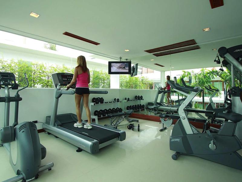 Moderner Fitnessraum mit Laufband, Gewichten, Fahrradergometer und großen Fenstern mit Grünblick.