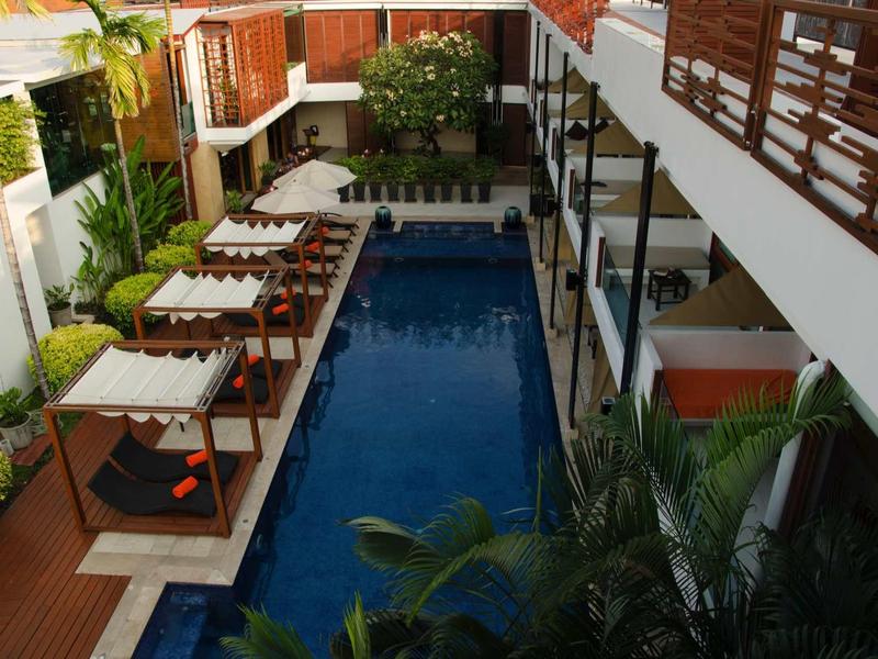 Moderner Innenhof mit rechteckigem Pool, Sonnenschirmen, Holzterrasse und grünen Pflanzen.