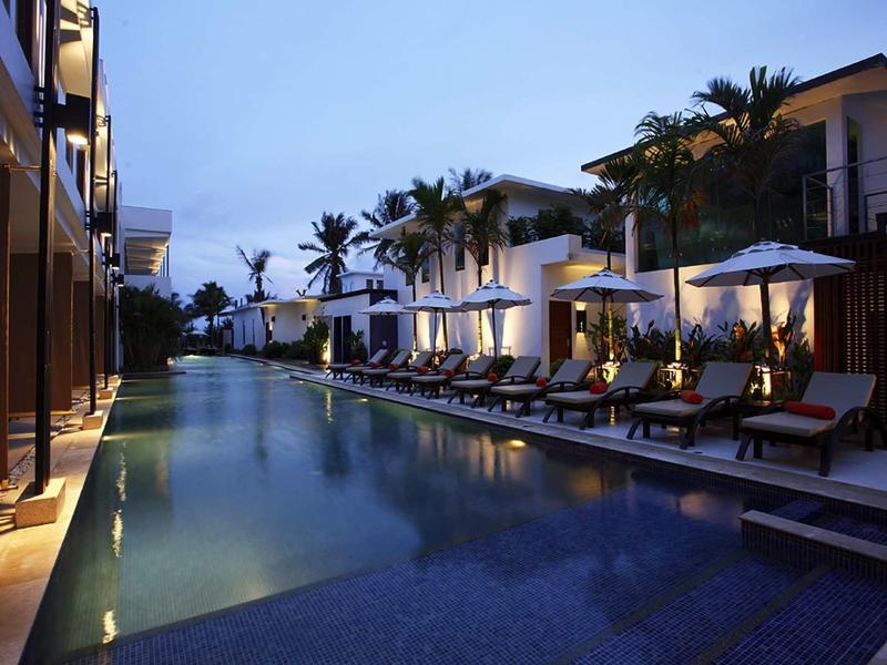 Moderner Poolbereich bei Dämmerung mit weißen Gebäuden, Liegen und Palmen an beiden Seiten.