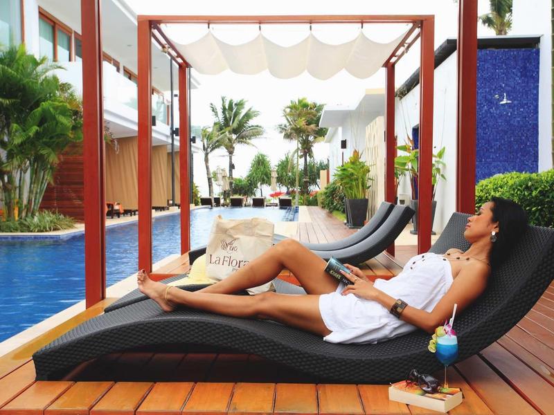 Frau entspannt auf schwarzem Liegestuhl am Pool, umgeben von Pflanzen und Holzterrasse.