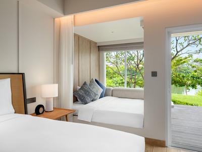 Lichte hotelkamer met twee bedden, raamzitje en uitzicht op tuin en meer.