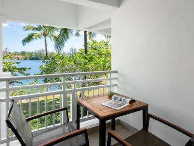 Balkon met tafel en twee stoelen met uitzicht op tropische planten en water.