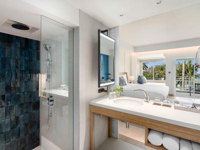 Moderne badkamer met glazen douche, grote spiegel en uitzicht op balkon en landschap.