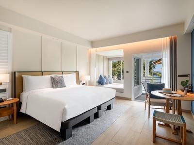 Modern hotelkamer met groot bed, bureau, fauteuil en balkon met uitzicht op groen