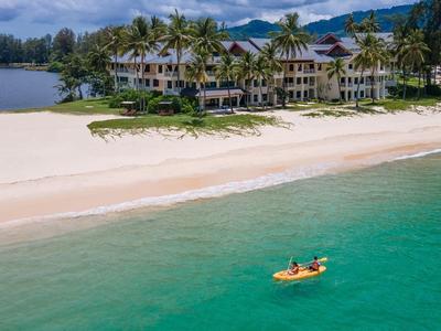 Resort tropical en playa de arena blanca con palmeras y dos kayakistas en agua clara.