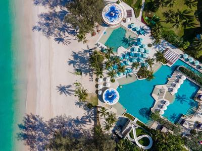 Vista aérea de un resort tropical con varias piscinas junto a una playa de arena blanca y mar turquesa.