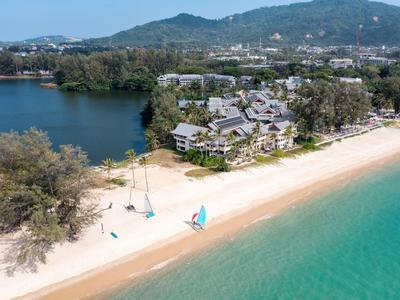 Strand met helder water en zeilboten voor een resort met bergen op de achtergrond