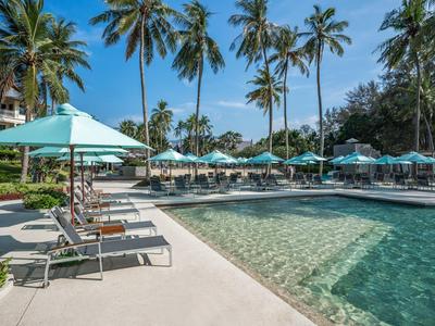 Zwembad met ligstoelen en parasols naast palmbomen onder een heldere lucht.