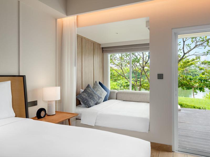 Lichte hotelkamer met twee bedden, raamzitje en uitzicht op tuin en meer.