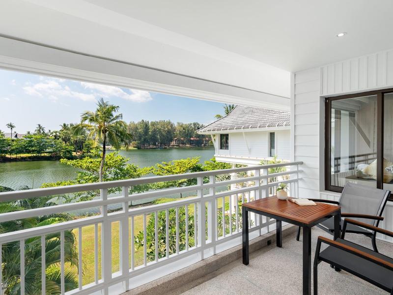 Balkon met tafel en stoelen met uitzicht op groene tuin en watergebied bij daglicht.