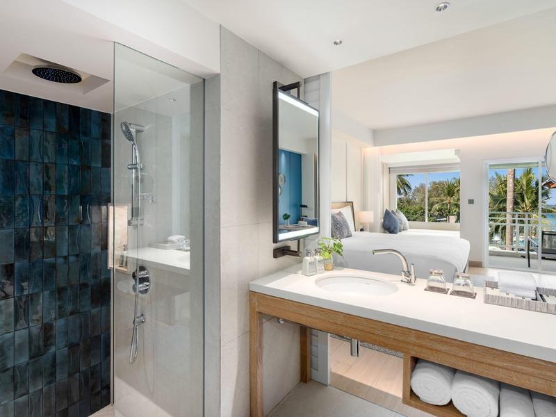 Moderne badkamer met glazen douche, grote spiegel en uitzicht op balkon en landschap.