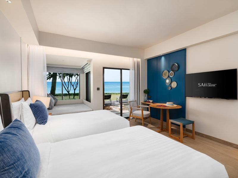 Modern hotelkamer met twee bedden, zithoek en uitzicht op zee.