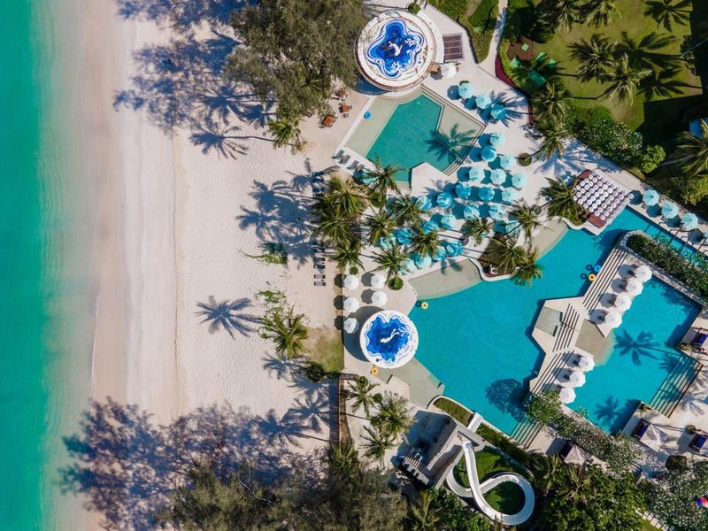 Luchtfoto van een strandresort met zwembaden, palmbomen en fijn zandstrand