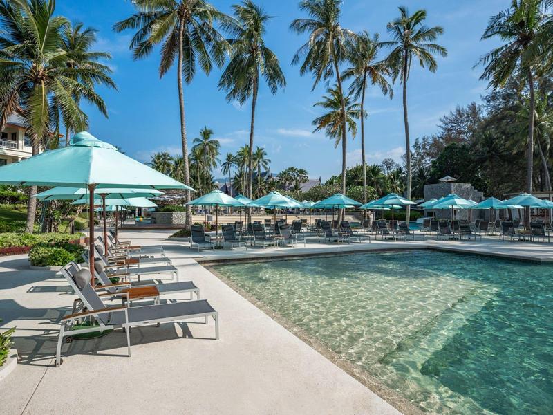 Zwembad met ligstoelen en parasols naast palmbomen onder een heldere lucht.