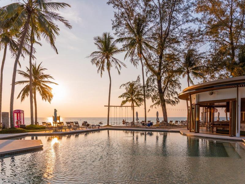 Een zonsondergang boven een infinity-zwembad met palmbomen en zeezicht in een tropisch resort.