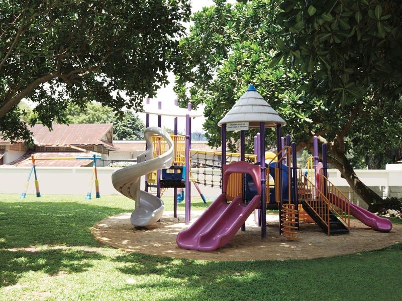 Kinderspeelplaats met glijbanen en klimrekken op een groen grasveld onder bomen.