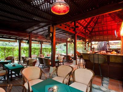 Offenes Restaurant mit Holzdach, weißen Stühlen und grünen Tischtüchern, warm beleuchtet.