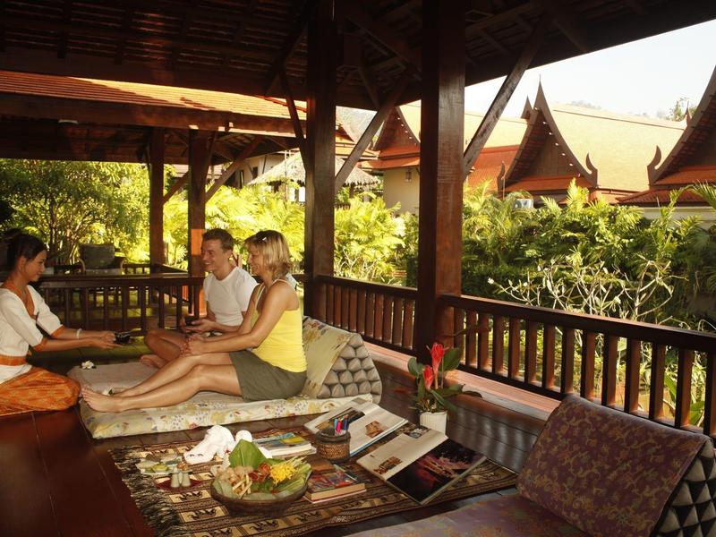 Ontspannen gasten zittend op comfortabele kussens in een open Thaise paviljoen met traditionele architectuur.