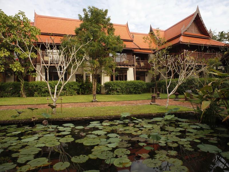 Traditioneel Thais gebouw met rood dak en vijver met waterlelies op de voorgrond.