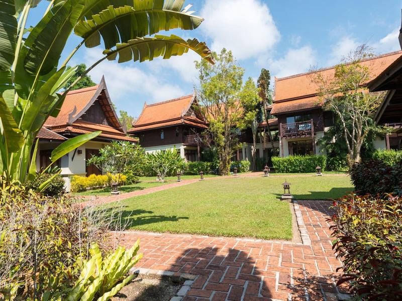 Een hotel met traditionele architectuur, rode daken en een verzorgde tuin onder een blauwe lucht.