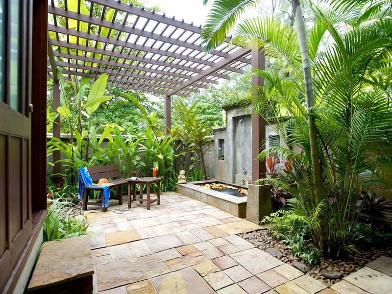 Groene tuin met tafel, stoelen en schaduwrijke pergola naast hotelkamer.