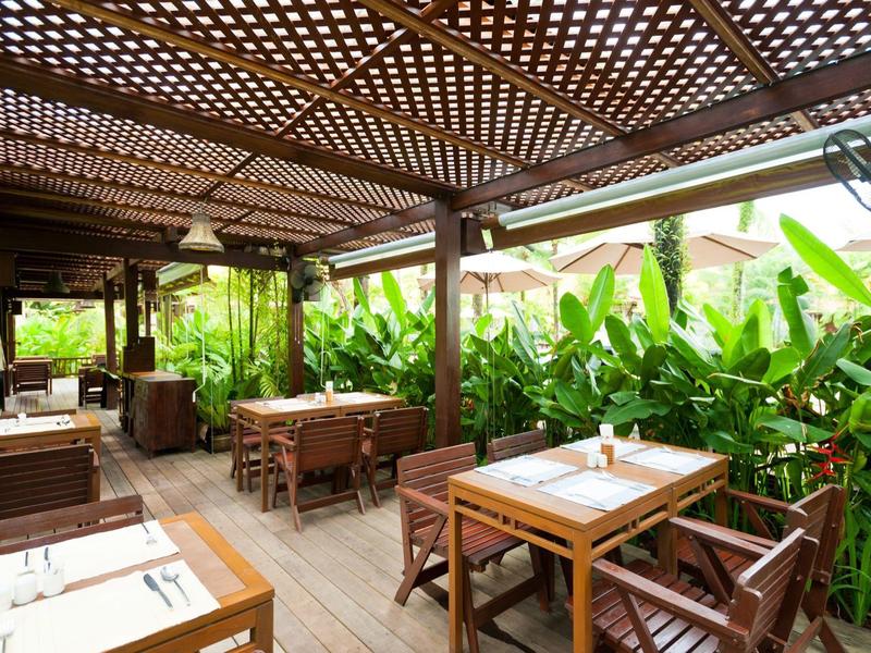 Open restaurantgedeelte met houten tafels en groene planten onder een houten dak.