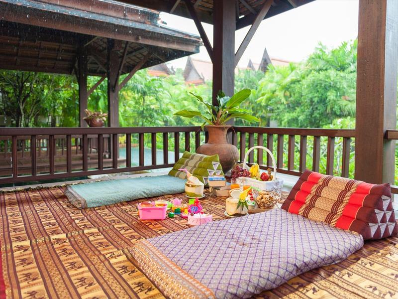 Gezellige buitenlounge met kussens en snacks in een houten veranda omgeven door bamboe.