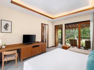 Modern hotel room with large bed, desk, TV, and terrace overlooking greenery.