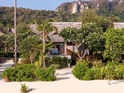 Tropical resort with bungalows, lush greenery, and sandy path under blue sky