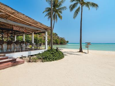 Strandrestaurant mit Blick auf weißen Sandstrand, Palmen und blaues Meer bei klarem Himmel.