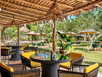 Covered outdoor lounge with tables, chairs, and view of garden and umbrellas