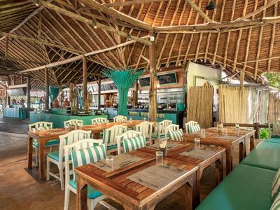 Offenes Restaurant mit Holzdach und Holztischen neben grünen Sitzbänken.