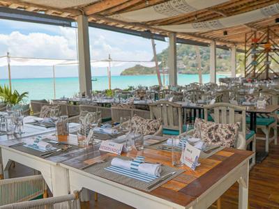 Offenes Restaurant mit Blick auf das Meer und Klippen, gedeckte Tische und heller Holzboden.