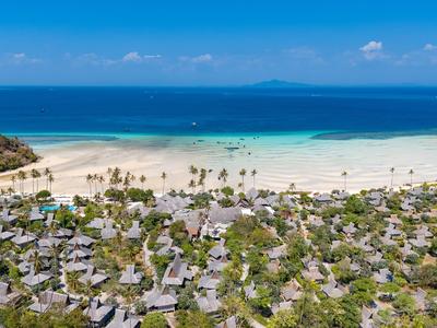 Resort mit zahlreichen Bungalows an einem weißen Sandstrand und blauem Meer.