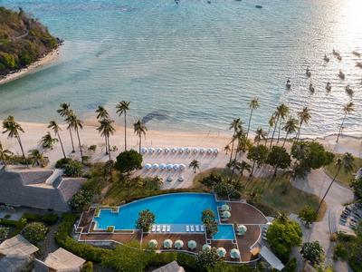 Aerial view of a tropical beach with palm trees, a pool, and sun loungers at the hotel