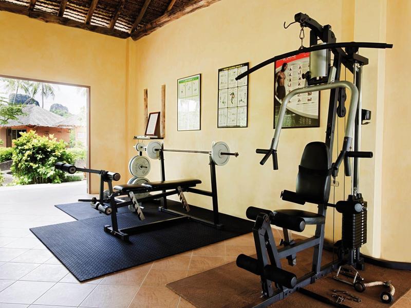 Small home gym with weights and multi-function strength machine in bright room.