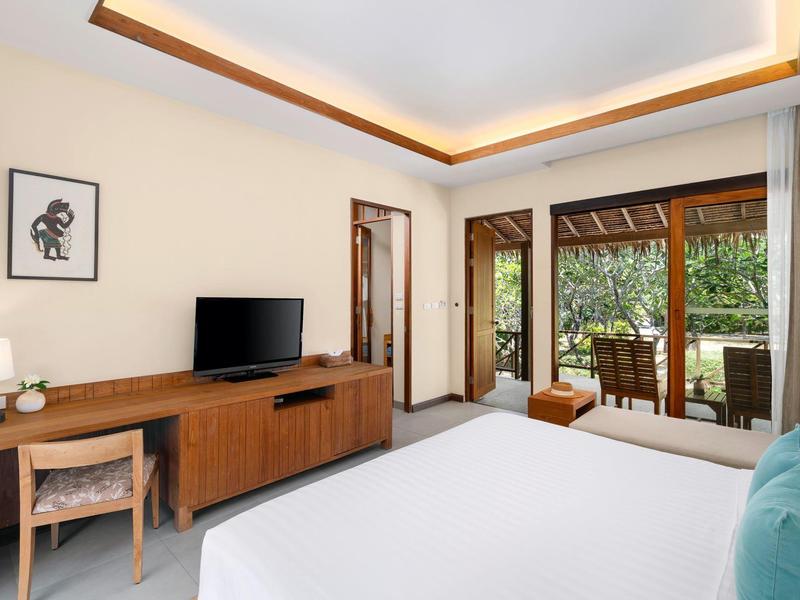 Modern hotel room with large bed, desk, TV, and terrace overlooking greenery.