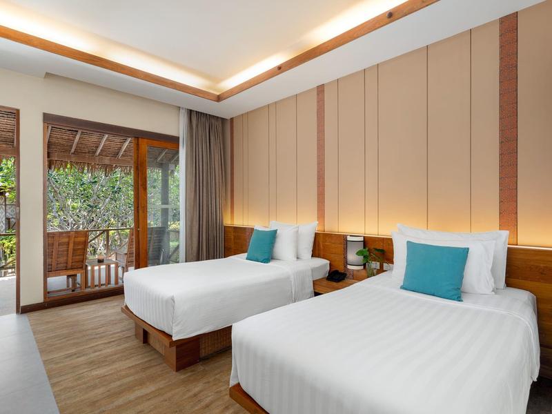 Modern hotel room with two single beds, wooden floor, and terrace overlooking greenery.