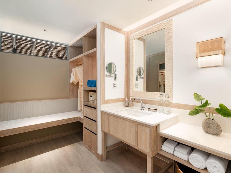 Bright, modern dressing area with bench, mirror, and open wardrobe in hotel room.